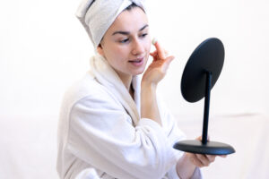 A young woman applies cream on her face, looks in the mirror.